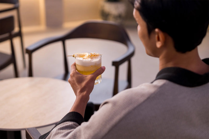 Person holding Leona My Honey cocktail in a cozy lounge setting at Leona Onsen.